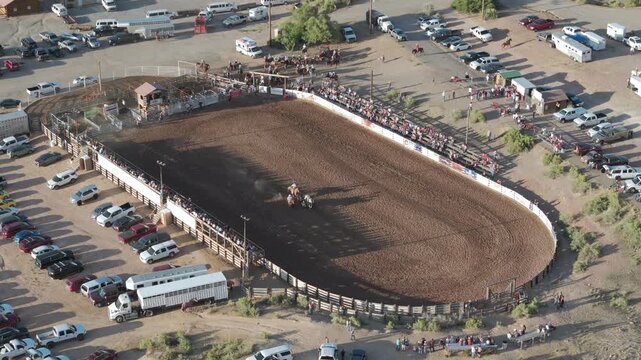 Fruita, United States - 25 July 2025: Aerial view of a vibrant rodeo arena, teeming with life and framed by parked cars and cheering spectators.