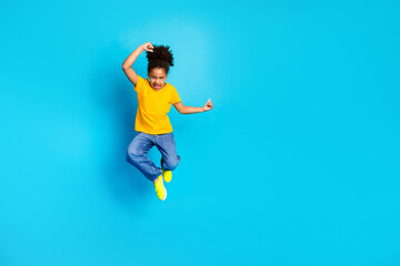 Joyful young girl wearing yellow t-shirt jumping in excitement against a vibrant blue background