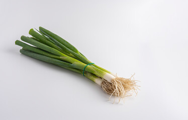 Fresh green onions with roots tied in a bunch on white background.

