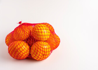 Bright oranges in red mesh bag, isolated on white background.
