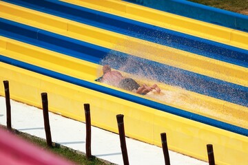 A person speeds down a brightly colored yellow and blue water slide, creating a splash of water....