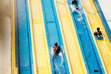 People descend a vibrant blue and yellow water slide at a water park. Individuals are splashing...