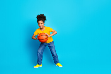 Excited young girl holding a basketball on a vibrant blue background showcasing energy and youthful fun
