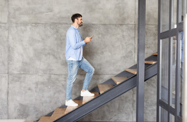 This image shows a man walking up a modern staircase in a home. The man is casually dressed in a...