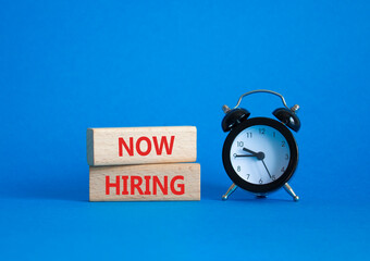 Now Hiring symbol. Wooden blocks with words Now Hiring. Beautiful blue background with alarm clock. Business and Now Hiring concept. Copy space.