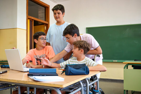 Group of elementary school students collaborating with a laptop in classroom setting, including a boy in wheelchair - Powered by Adobe
