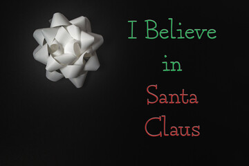 White gift bow on dark background with festive text expressing belief in Santa Claus