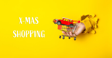 Hand holding shopping cart with toy car on bright yellow background for festive shopping concept
