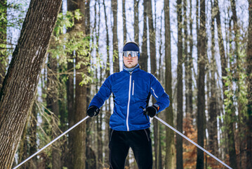 Male athlete taking a break during cross-country skiing training in a serene, snowy forest, soaking in the tranquil winter landscape and breathing in the crisp, fresh air