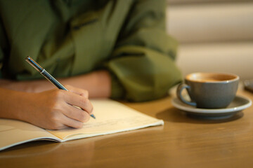 Woman writing down her thoughts on notebook at cafe, work space concept.