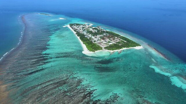 Aerial view of an island with lush green trees and buildings contrasting against the turquoise waters and surrounding reef, Naavaidhoo, Haa Dhaalu City, Maldives.