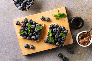 Sweet homemade toasts with chocolate paste, nuts, blueberry and aromatic mint leaves on the serving...