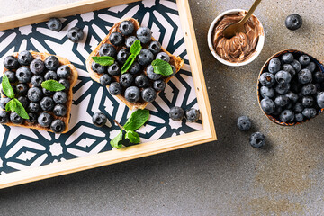 Sweet homemade toasts with chocolate paste, nuts, blueberry and aromatic mint leaves on the serving...