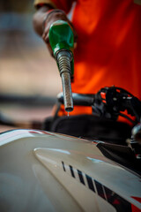 Green nozzle refueling white motorcycle tank close-up.Tight close-up of green fuel nozzle inserted...