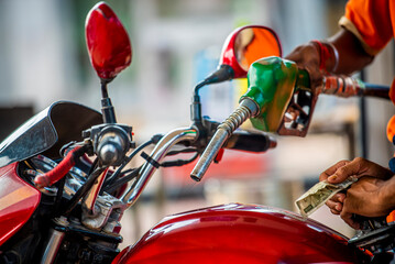 Green petrol nozzle refueling red motorcycle in India. Indian petrol pump staff filling red...