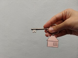 Hand holding a silver key with house shape keychain. Housing and property investment concept. House key.