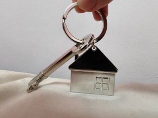 Hand holding a silver key with house shape keychain. Housing and property investment concept. House key.