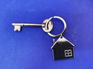 A silver key with house shape keychain isolated on blue background. Housing and property...