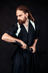 Samurai warrior in traditional Japanese clothing holding a katana sword in a dramatic pose on a dark studio background. Concept of martial arts, Japanese culture, and ancient warriors.