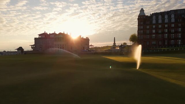 Aerial view of the lush green fairways of The Old Course as sprinklers shower the landscape, contrasting with the grand hotels, St Andrews, Scotland, United Kingdom.