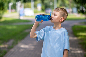 Teenage boy drinking water from sports bottle outdoors on a warm sunny day