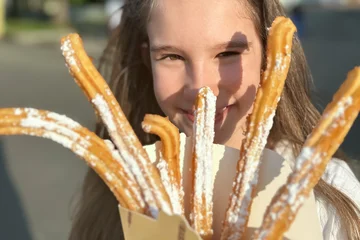 Gordijnen Cute little caucasian smiling girl eating traditional Spanish fast food churros with caramel outdoors. Sunny positive picture © Nikolay N. Antonov
