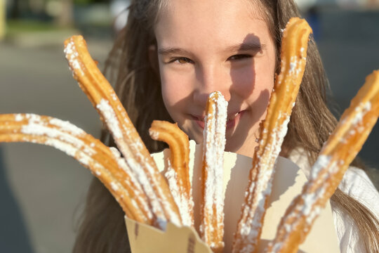 Fototapeta Cute little caucasian smiling girl eating traditional Spanish fast food churros with caramel outdoors. Sunny positive picture