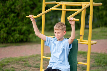 Blond boy working out on street gym equipment in the park
