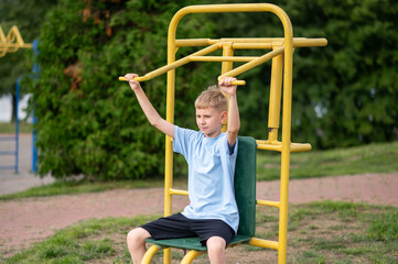 Teen boy training on outdoor fitness machine in summer park