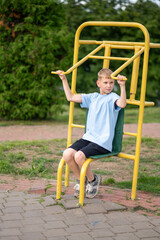 Blond boy working out on street gym equipment in the park