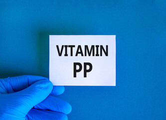 Vitamin PP symbol. Concept words Vitamin PP on beautiful white card. Doctor's hand in blue medical glove. Beautiful blue background. Medical healthy lifestyle Vitamin PP concept.