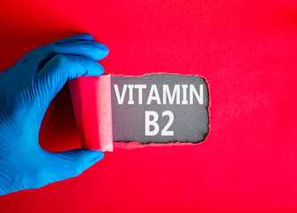 Vitamin B2 riboflavin symbol. Concept words Vitamin B2 on beautiful grey paper. Doctor hand in blue medical glove. Beautiful red background. Medical healthy lifestyle Vitamin B2 riboflavin concept.