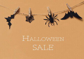 Halloween-themed decorations with bats, spider, and web hanging on a string against orange...