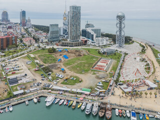 Aerial view of modern architecture meeting the sea, juxtaposing the Alphabet Tower with the Ferris wheel, bathed in soft light, Batumi, Adjara, Georgia.