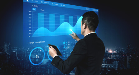 A businessman focuses on a digital screen displaying graphs and charts, showcasing data analysis in a modern office setting at night. Impute