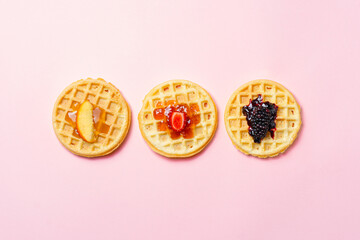 Three waffles with fruit toppings on pink background. Minimalist breakfast concept.