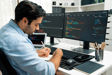 Smart IT developer writing data memo's software development on paper's coding on laptop and two pc...