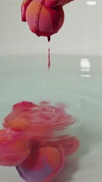 A hand releases a vibrant bath bomb into a tub, triggering a colorful, effervescent eruption: Watch as the water fizzes and bursts with brilliant hues and playful bubbles.