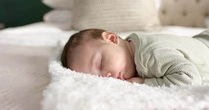 After falling asleep, newborn infant is lying on blanket with cream pillow, breathing gently