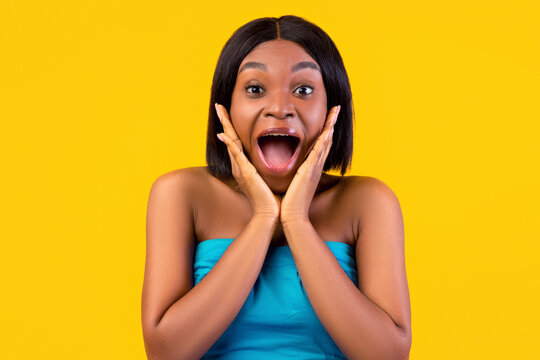 Omg. Excited African American woman in summer dress shouting in excitement, holding hands near face, posing over orange studio background. Summertime surprise, seasonal sale concept