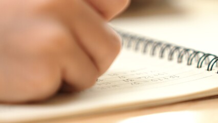 Close up of child hand taking a note or writing a letter at classroom. Happy student hands hold pen at book or doing homework or doing test at elementary school. Focus on hand. Education. Pedagogy.