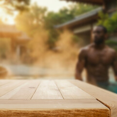 Empty wooden platform with copy space for product, blurred man relaxing in thai garden and spa in background. Japanese-style garden with lush greenery, pools, and elements of serene spa retreat. 