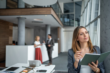 Businesswoman planning strategy, holding notebook and pen in modern office