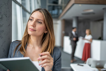 Businesswoman holding notebook and pen, thinking by the window in office