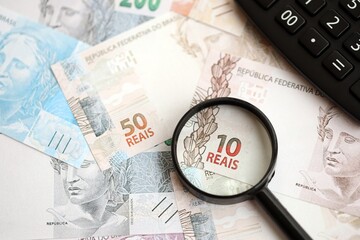 Brazilian reais banknotes and calculator with magnifying glass. Brazil real money, calc with loupe