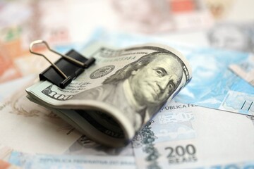 Bunch of US dollar bills lies on big amount of Brazilian reais banknotes close up