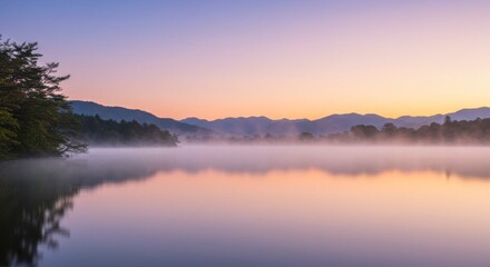 Fototapeta premium Tranquil misty lake scene at dawn, with mountains in the background and trees. Soft light over water