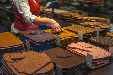 Sale of various thin chocolates. Stacks of chocolate sheets in various flavors being handled by vendor in red vest. Concept of chocolate, handmade sweets, gourmet confections