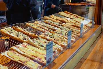 Pizza display case. Baked baguette pizzas topped with melted cheese and various toppings displayed...