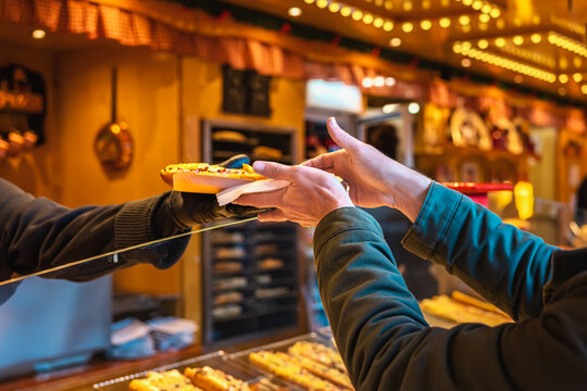 Customer receiving hot food from market vendor over counter at festive food stall, halve of small baguette with cheese and other things. Concept of street food, fast service, culinary interaction